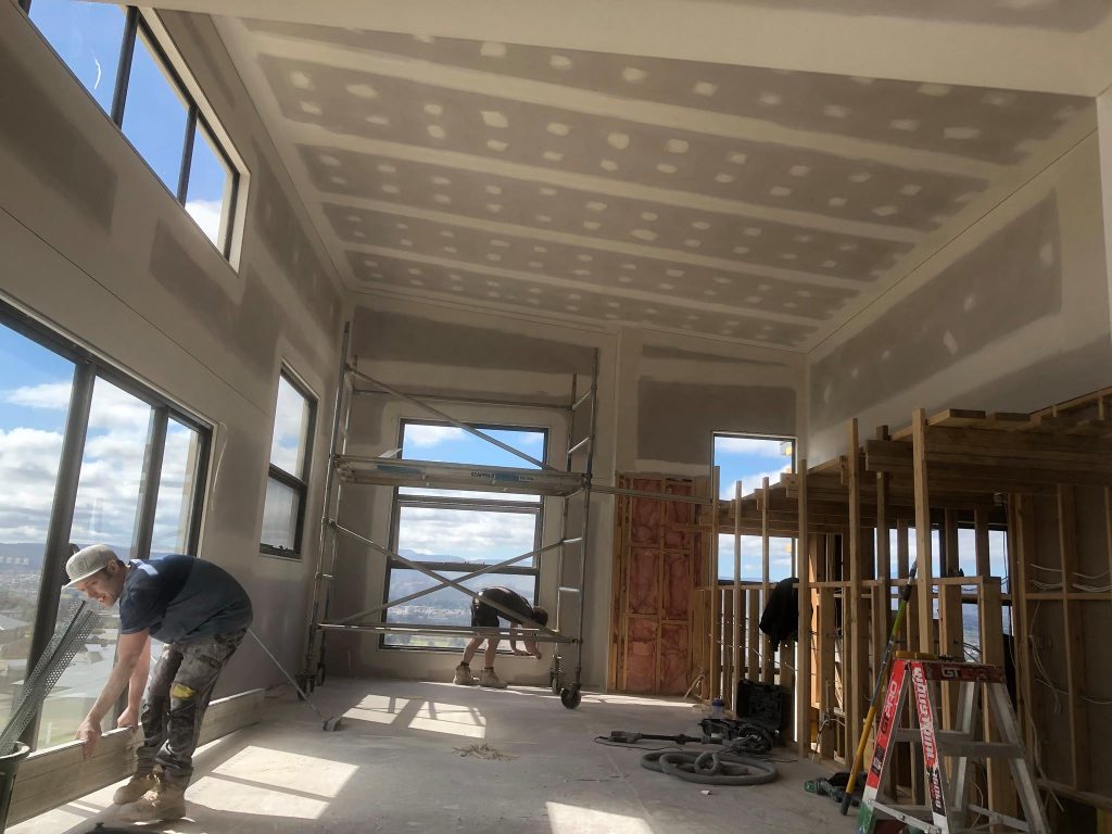 Workers in a high-ceilinged room with set plasterboard, scaffolding and timber framing